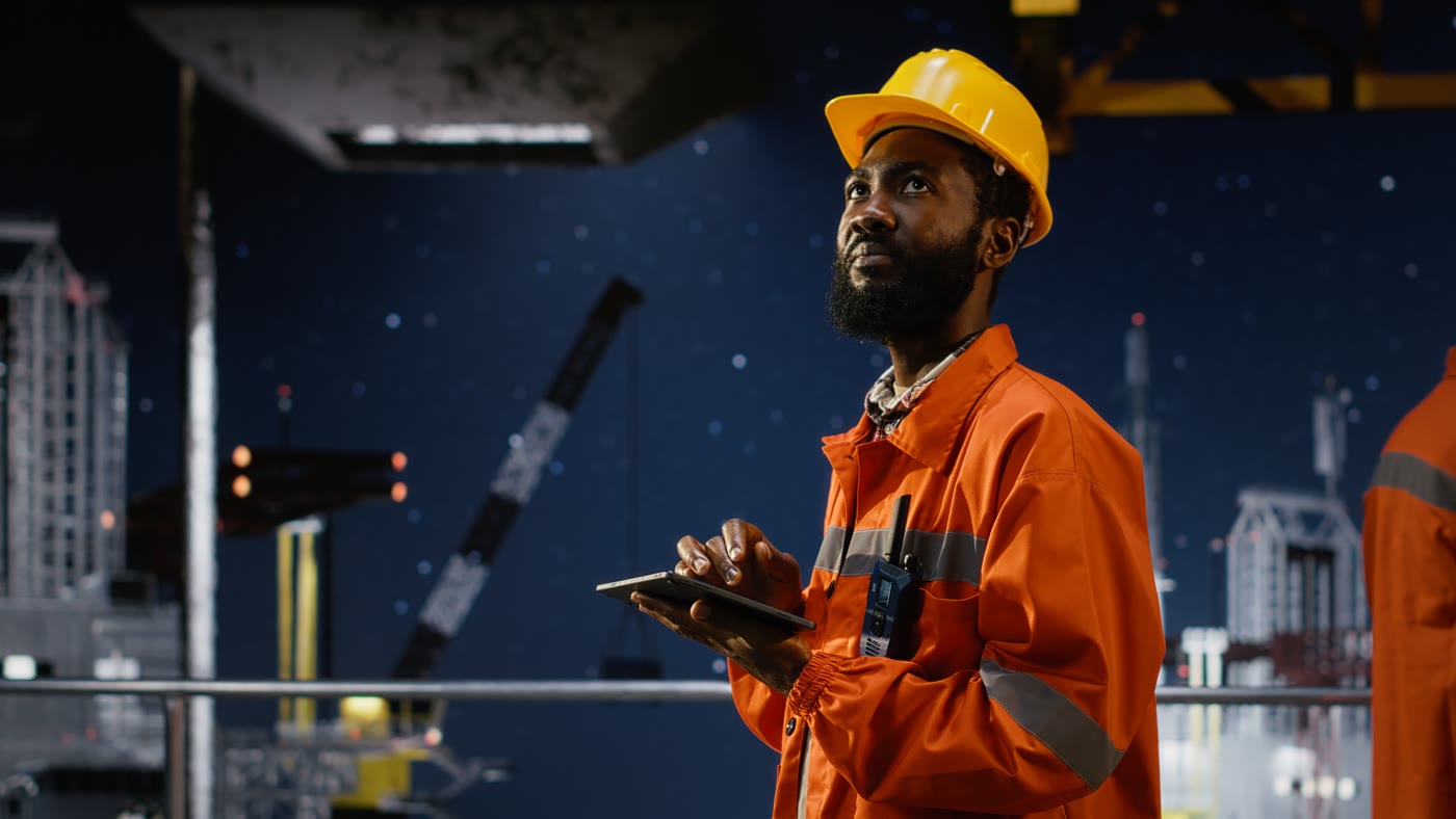 Engineer using a tablet to monitor offshore systems at a night-time industrial site