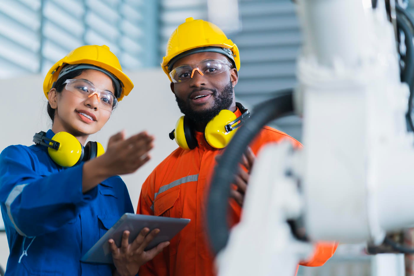 Two technicians in full PPE (hard hats, safety glasses and ear defenders) inspecting industrial valve equipment