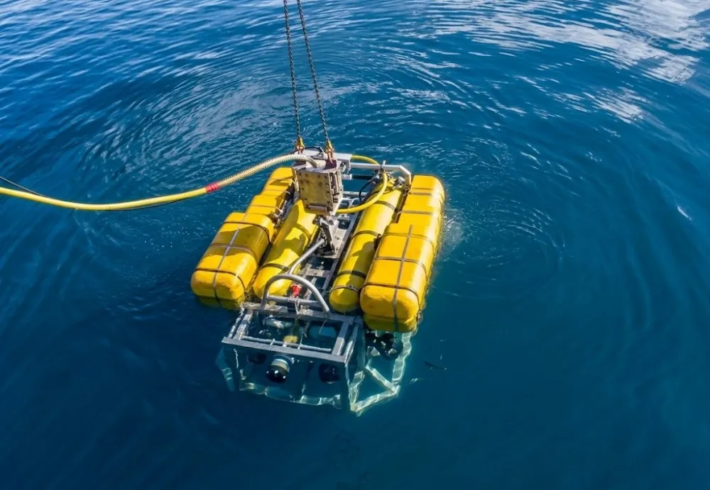 Aerial view of a remotely operated vehicle (ROV) being lowered into the water from a support vessel
